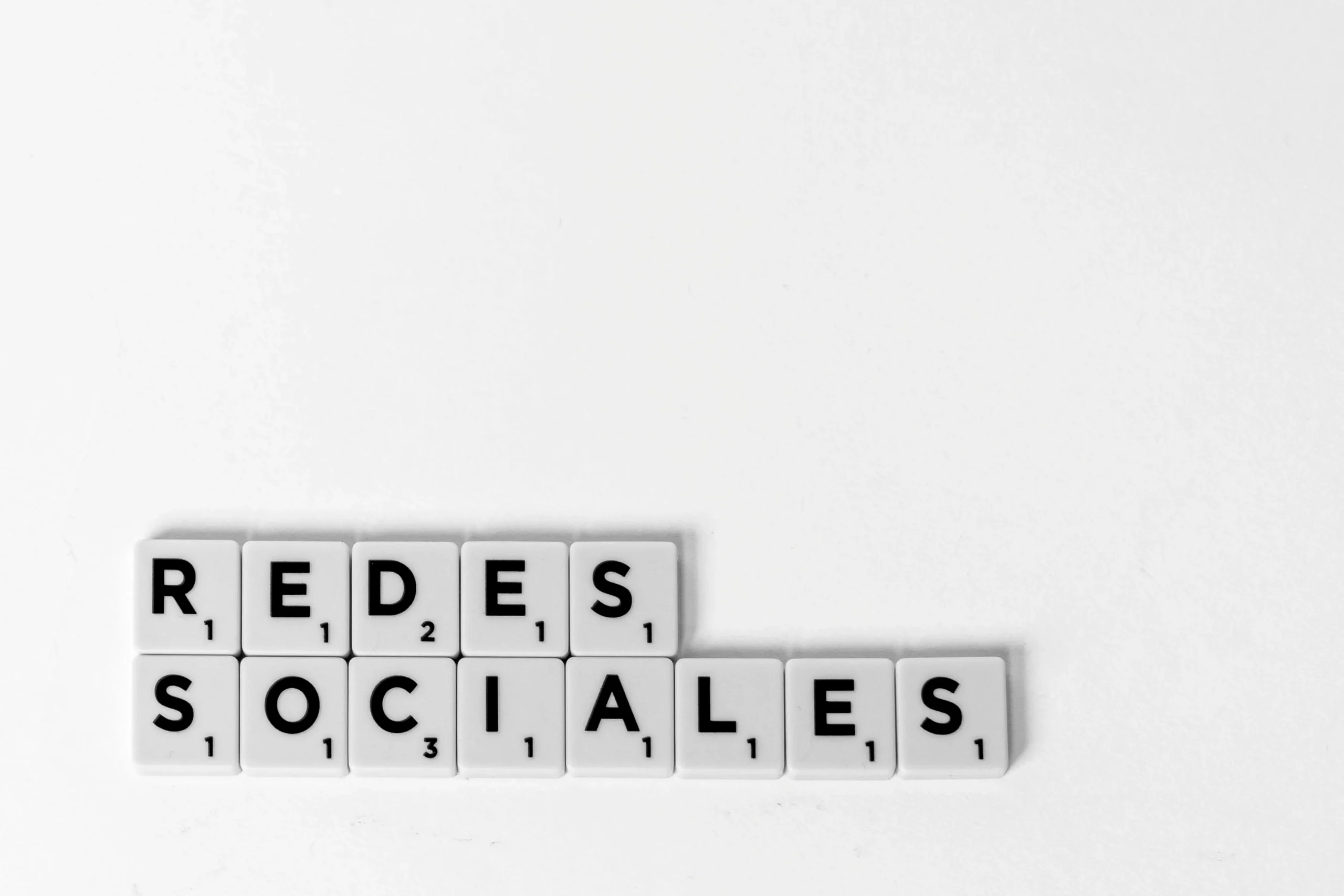 "Redes Sociales" (Social Networks) spelled out with Scrabble tiles on white surface.